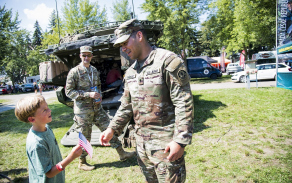 Americký voják předává vlajku USA před obrněným transportérem Stryker.